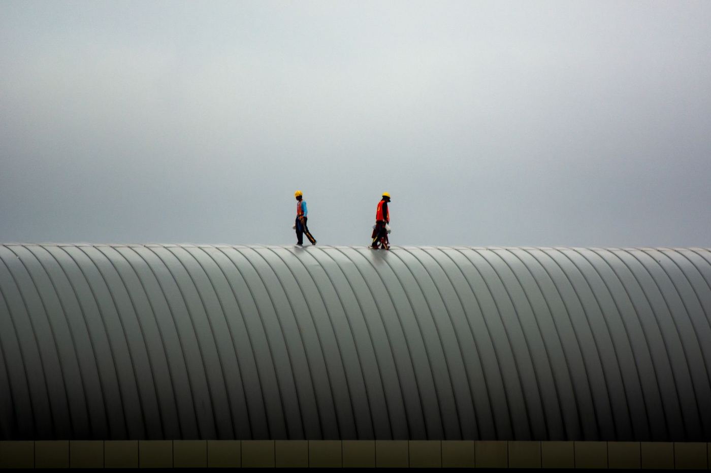 Two roofers walking a curved metal roof